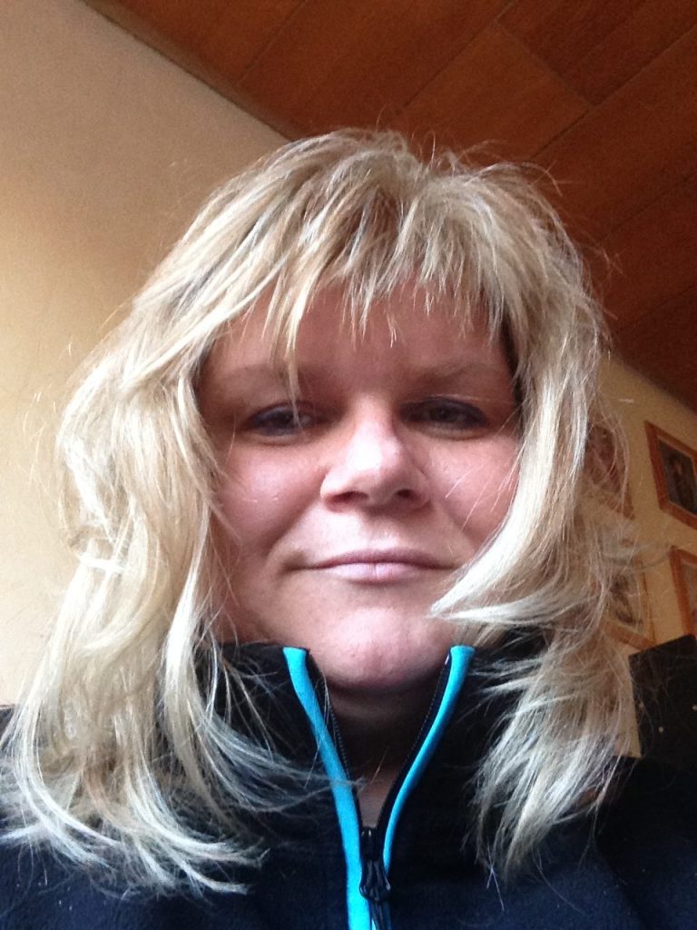 Porträt einer Frau mit blondem, leicht lockigem Haar, die lächelt. Sie trägt einen schwarzen Pullover. 
